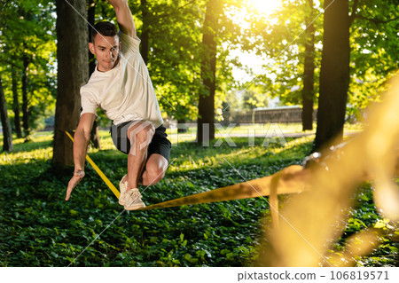 Sportsman on the rope practising slacklining and looking concentrated Sportsman on the rope practising slacklining and looking concentrated 106819571