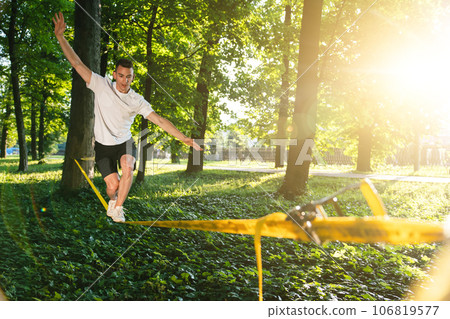 Young man in white tshirt and shorts on the rope keeping balance Young man in white tshirt and shorts on the rope keeping balance 106819577