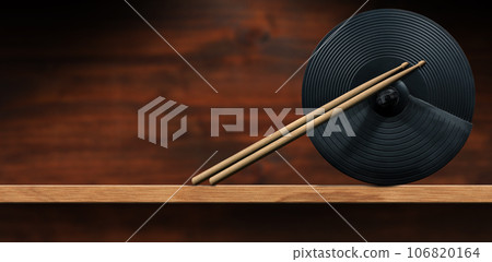 Black Cymbal of an Electronic Drum Kit and a Pair of Wooden Drumsticks 106820164