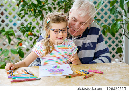 Happy positive cute little preschool girl and handsome senior grandfather painting with colorful pencils at home. Grandchild and man having fun together Happy positive cute little preschool girl and handsome senior grandfather painting with colorful pencils at home. Grandchild and man having fun together 106820215