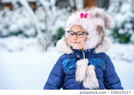 Portrait of a cute little girl in a hat and scarf in winter. preschool child with glasses in the forest. Happy child in winter clothes Portrait of a cute little girl in a hat and scarf in winter. preschool child with glasses in the forest. Happy child in winter clothes 106820217