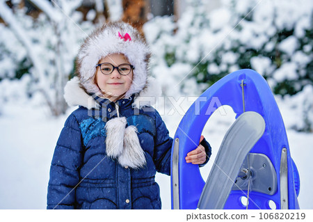 Little girl enjoying a day out playing in the winter forest. Portrait of cute preschool child with glasses with sled. Kid having fun. 106820219