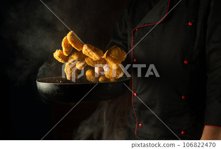 Cooking crispy nuggets. The chef tosses hot nagits into the pan. The concept of a large kitchen for a hotel with an advertising space Cooking crispy nuggets. The chef tosses hot nagits into the pan. The concept of a large kitchen for a hotel with an advertising space 106822470