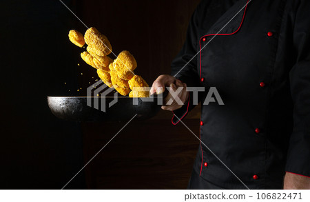 The chef prepares crispy nagits in a steamed hot pan. Flying nagits over the frying pan in the cook hand. Place for prescription on black background The chef prepares crispy nagits in a steamed hot pan. Flying nagits over the frying pan in the cook hand. Place for prescription on black background 106822471