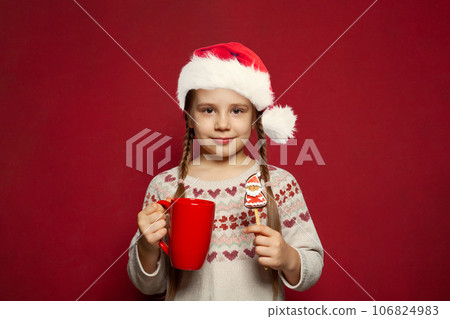 Happy Xmas child wearing red Santa hat with ginger cookies and Christmas drink standing Happy Xmas child wearing red Santa hat with ginger cookies and Christmas drink standing 106824983