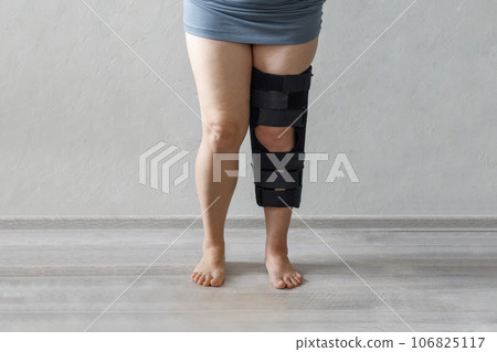 Black medical knee pad with a fixator on female knee at grey background 106825117