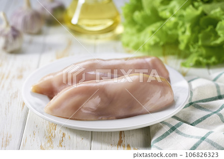 Raw chicken breast with salt, garlic and fresh herbs on a white table. Healthy food. Raw chicken breast with salt, garlic and fresh herbs on a white table. Healthy food. 106826323