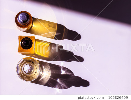 Yellow cosmetic bottles with essential oil on white table top view. Contrasting shadows. Spa treatment, wellness, body, face care. Beautiful minimalistic composition flatly. Beauty products copy space 106826409