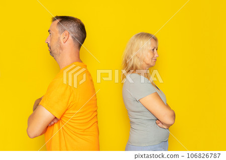 Portrait of a real Caucasian couple in their 40s having an argument, they are angry and turn their backs on each other. Isolated on yellow background. Portrait of a real Caucasian couple in their 40s having an argument, they are angry and turn their backs on each other. Isolated on yellow background. 106826787