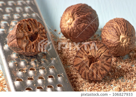 A group of nutmeg nuts and a metal grater on a background of a light blue table with grated nutmeg powder A group of nutmeg nuts and a metal grater on a background of a light blue table with grated nutmeg powder 106827933