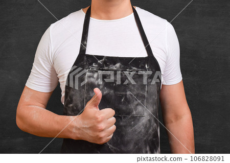 Cropped view of male cook pointing thumb up on black background. Cropped view of male cook pointing thumb up on black background. 106828091