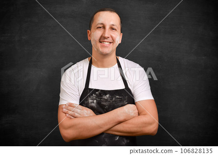 Confident young man in apron looking at camera on dark background. 106828135