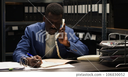 In incident room, police officer answers landline phone, getting fresh case information and forensic evidence report in order to apprehend culprit. Private investigator on phone with a criminologist. 106830052