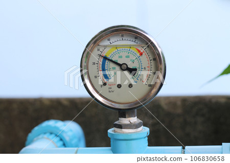 Circular water pressure meter attached to blue PVC water pipe to measure tap water pressure. 106830658