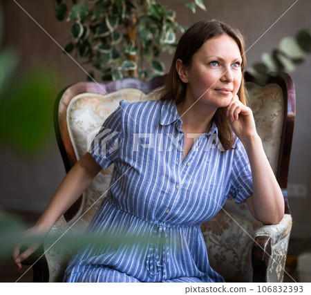 Girl is sitting in semi-dark room among indoor plants of ficus trees and remembers plot of book 106832393