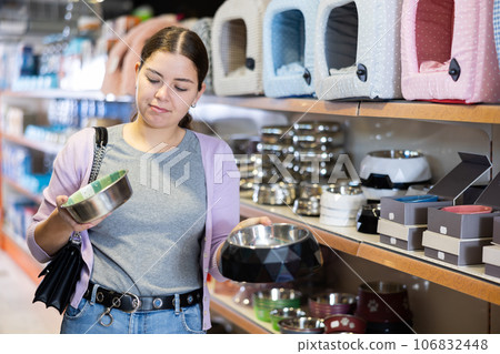 Young cheerful woman buying bowl for pets in pet store Young cheerful woman buying bowl for pets in pet store 106832448