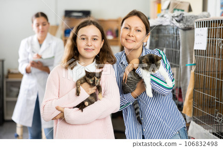 Tween girl with mother holding adopted kittens in animal shelter 106832498
