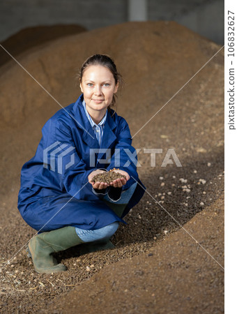 Joyful woman farmer at heap of rapeseed oil cake, animal food Joyful woman farmer at heap of rapeseed oil cake, animal food 106832627
