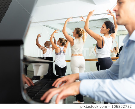 Ballet students doing exercises near barre with musician at piano 106832782