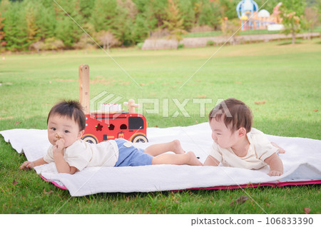 Twins, children, and babies lying on the grass and playing 106833390