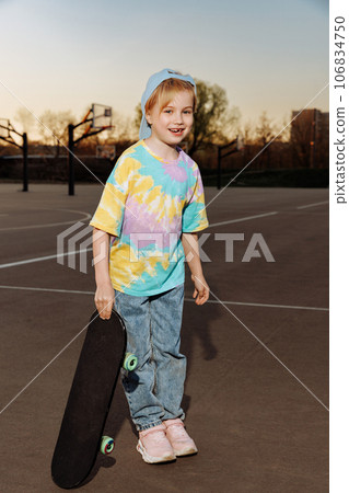 Fashionable child girl in casual clothes and jeans stands with skateboard Fashionable child girl in casual clothes and jeans stands with skateboard 106834750