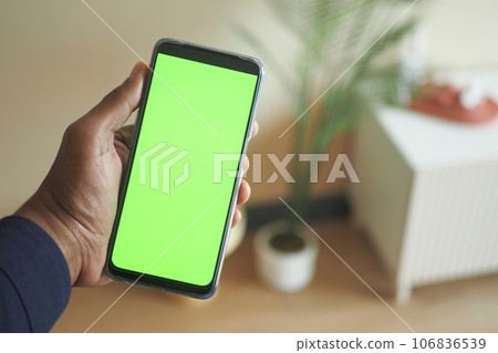 holding smart phone with green screen and home interior decoration on table holding smart phone with green screen and home interior decoration on table 106836539