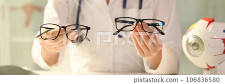 Ophthalmologist holds different eyeglasses in her hands while sitting at desk in medical clinic. Ophthalmologist holds different eyeglasses in her hands while sitting at desk in medical clinic. 106836580