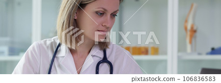 Female doctor holds clipboard with documents and works at computer in medical office. Female doctor holds clipboard with documents and works at computer in medical office. 106836583