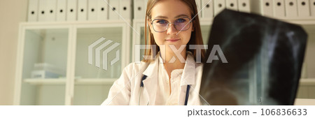 Young doctor in glasses holds chest x-ray and looks at camera. Young doctor in glasses holds chest x-ray and looks at camera. 106836633