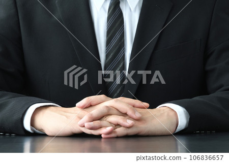 一個穿著西裝的男人在辦公桌前交叉手指 106836657