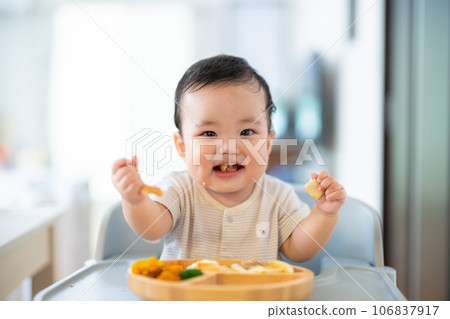 A 9-month-old baby who is in a good mood after grabbing and eating in the late stage of baby food 106837917