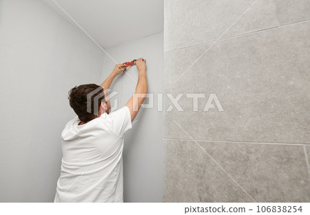 Male worker using spirit level tool and pencil while checking wall level before repair works. Man measuring white wall with construction level ruler and drawing line. Home renovation concept. 106838254