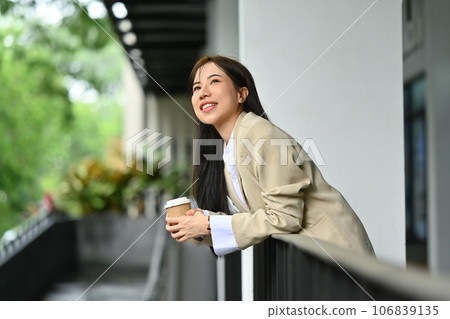 Beautiful 30s businesswoman holding takeaway coffee cup and enjoying nature view from a balcony 106839135