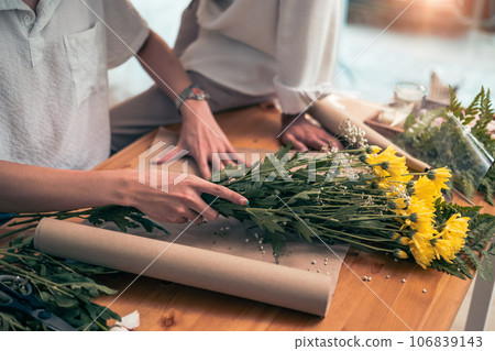 Male florist wrapping flowers on wooden table at hid flower shop. Small business concept 106839143