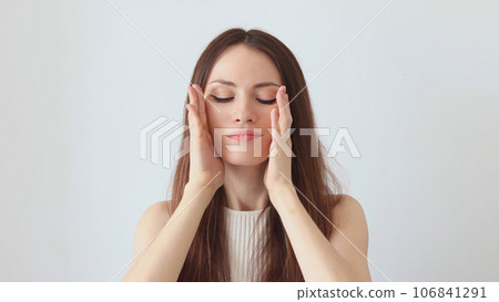 A beautiful woman gives a facial massage with her hands A beautiful woman gives a facial massage with her hands 106841291