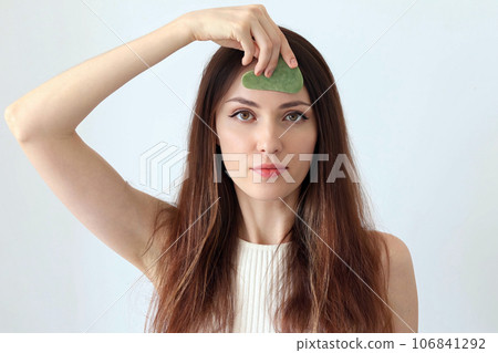 Close-up portrait of a beautiful girl, red-haired woman massaging her face with a stone scraper 106841292