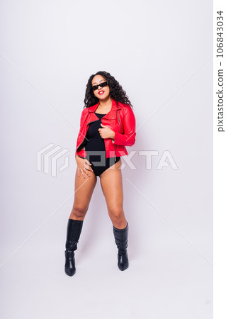 African American curvy female in black bodysuit and jacket on red and white background in studio 106843034