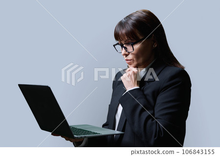Serious mature woman using laptop, on grey background 106843155