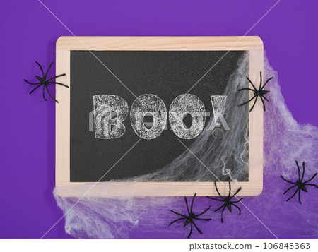 Black chalkboard with text boo, white cobwebs and black spiders on a purple background. A place for your text. Black chalkboard with text boo, white cobwebs and black spiders on a purple background. A place for your text. 106843363