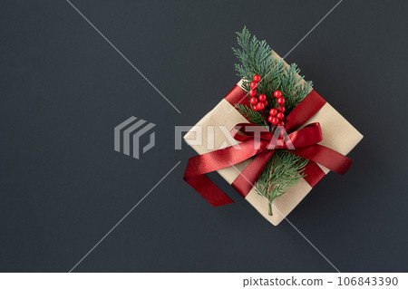 Banner with craft gift box with red ribbon and thuja sprig on a dark background. Banner with craft gift box with red ribbon and thuja sprig on a dark background. 106843390