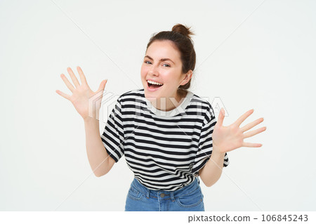 Image of happy, beautiful young woman makes jazz hands, surprise gesture, posing in casual t-shirt and jeans over white background 106845243