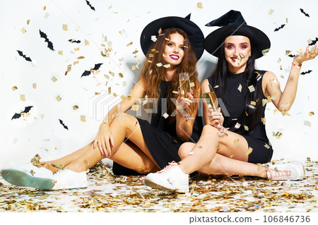 portrait of two happy young women in black witch halloween costumes. firecrackers in the background. portrait of two happy young women in black witch halloween costumes. firecrackers in the background. 106846736