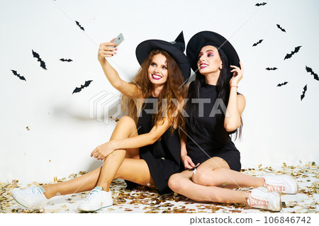 Portrait of two happy women in black witch halloween costumes on party over white background. Portrait of two happy women in black witch halloween costumes on party over white background. 106846742