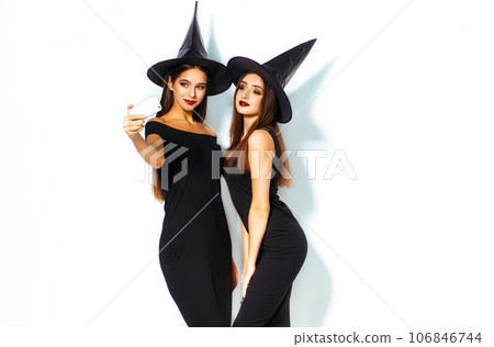 nice portrait of two beautiful young woman in black witch halloween costumes on party over white background. 106846744