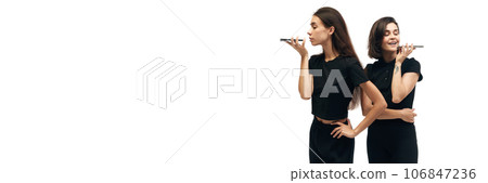 banner. Portrait of two young happy women wearing fashion outfit holding phones in hands orderind products isolated on white background. ad 106847236