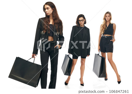 Season of sales concept. Full length portrait of three young attractive women in fashion outfit holding black bags in hands isolated white background Season of sales concept. Full length portrait of three young attractive women in fashion outfit holding black bags in hands isolated white background 106847261