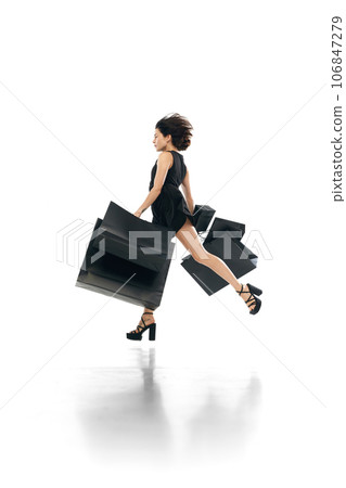 Black friday concept. Shopaholic. Side view portrait of woman wearing fashion mini black dress flying, running to shopping mall. 106847279