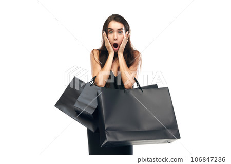 Black friday concept. Portrait of shocked woman wearing black dress raising hands with bags. Beginning season of sales. 106847286