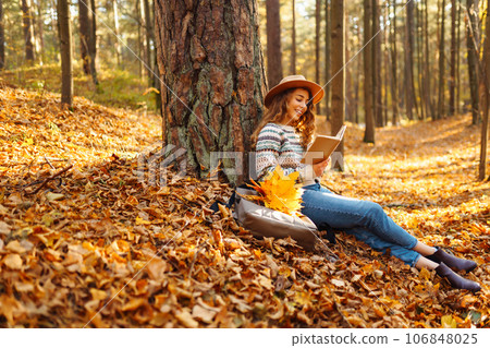 Stylish woman reading a book in the autumn park. Relaxation, enjoying, solitude with nature. Stylish woman reading a book in the autumn park. Relaxation, enjoying, solitude with nature. 106848025