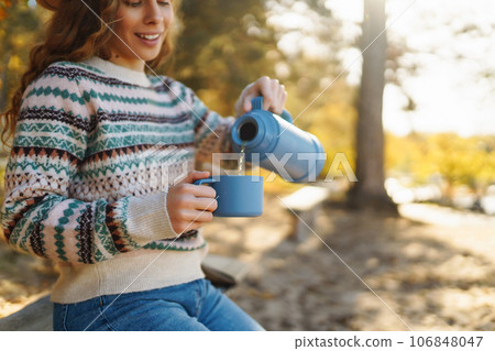 Woman holds thermos and drinks tea in sunny autumn forest. Vacation, travel, lifestyle concept. 106848047